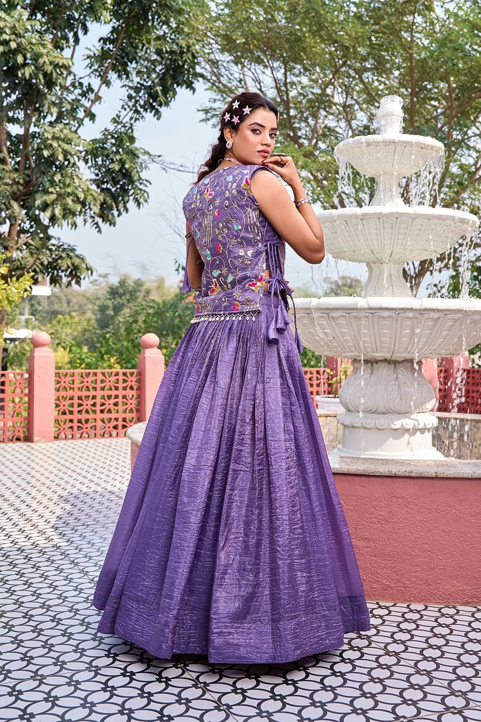 Woman in a purple dress standing in front of a fountain with trees in the background